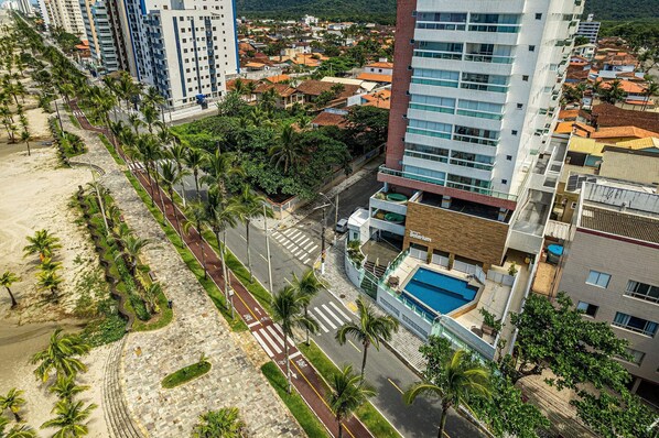 A high-rise hotel with a swimming pool, a beachside promenade, and a view of a residential area. - CANTINHO DA FAMÍLIA (Praia Grande)
