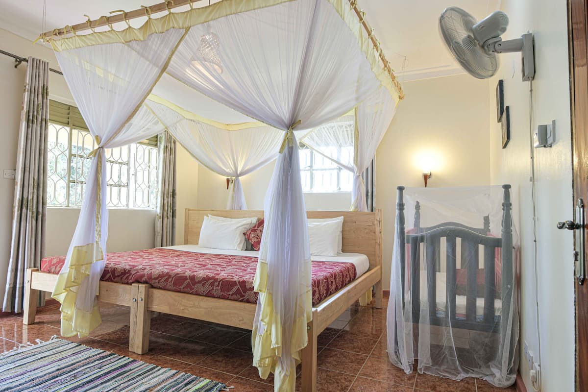 A room with a bed under a mosquito net, a fan, and a door with a gate.