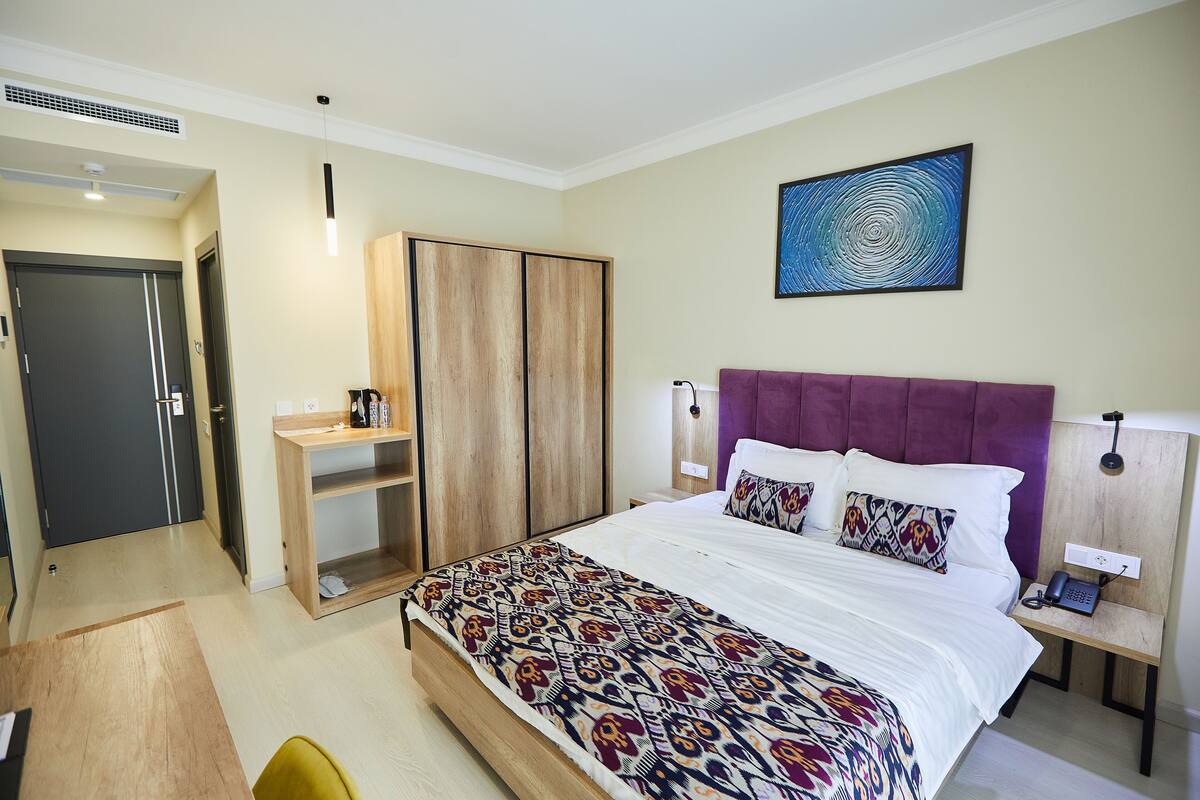 Una habitación de hotel con cama, escritorio, armario y un cuadro en la pared.