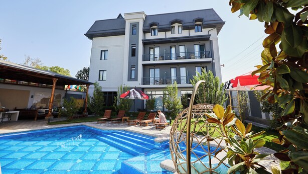 A pool area with lounge chairs and a building with multiple balconies in the background.