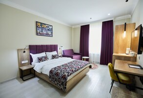 Moderni hotellihuone, jossa on sänky, työpöytä, tuoli ja pieni pöytä.