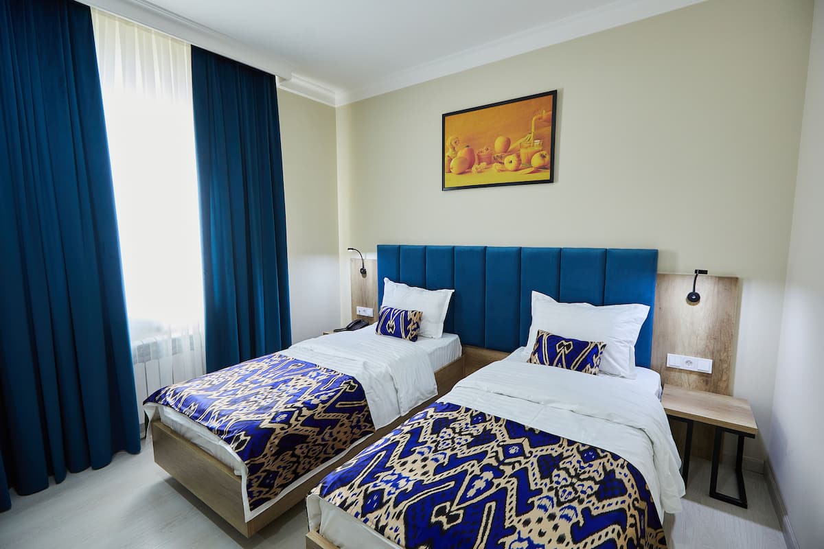 Habitación de hotel con dos camas, un ventanal con cortinas azules, un cabecero de madera y un cuadro en la pared.