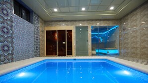 A swimming pool with a tiled pattern, a glass door entrance, and a shower area with blue lighting.