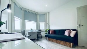 A modern living room with a desk, a green sofa, and a large window. - Apt. 07 - Beachside Beauty Central Studio Steps from Cafes (Brighton and Hove)