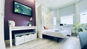 A modern bedroom with a bed, a desk with storage, a window, and a plant. - Apt. 07 - Beachside Beauty Central Studio Steps from Cafes (Brighton and Hove)