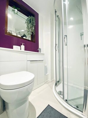 Un baño moderno con inodoro blanco, cabina de ducha con mampara de vidrio y pared de acento morada.