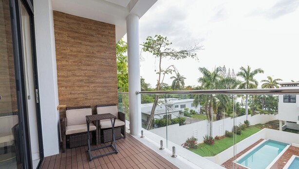 A balcony with a wicker sofa and table, a view of a swimming pool, and a brick patio.