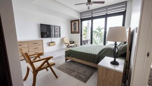 A bedroom with a bed, a desk, a chair, a TV, and a balcony view.