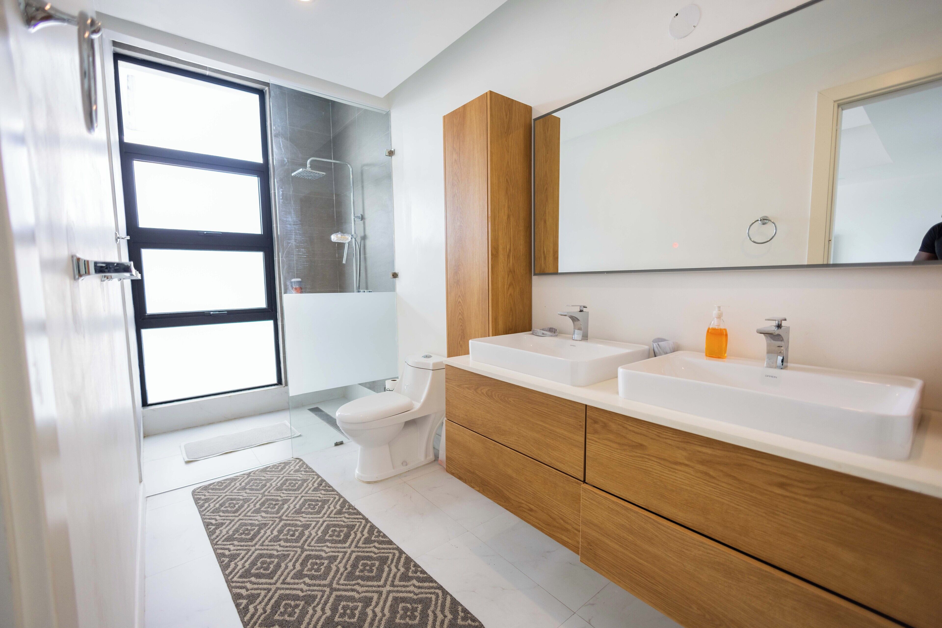 A modern bathroom with a large mirror, two sinks, and a toilet.