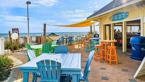 An outdoor patio with tables and chairs, a view of the ocean, and a building with a sign.
