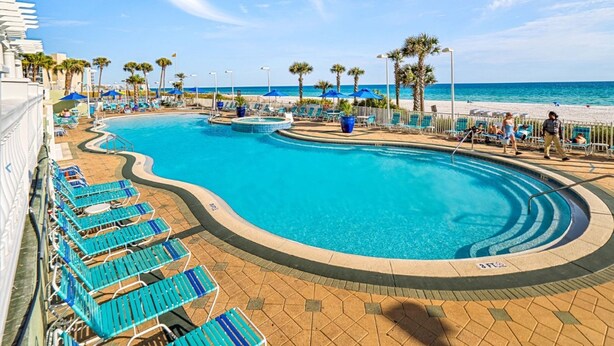 A pool area with blue lounge chairs and palm trees.