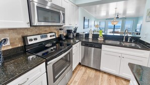 A modern kitchen with stainless steel appliances, a black granite countertop, and white cabinetry. - Ramsgate 31 - Gulf-Front Escape + Beach Service (Panama City Beach)