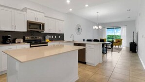 A modern kitchen with white cabinetry, a central island, and a dining area with a yellow chair. - New Discount Disney Lazy River TikiBar Balcony (Kissimmee)