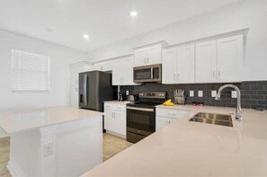 Enjoy cooking in this well-equipped kitchen with a central island, stainless steel appliances, and a black tiled backsplash.
