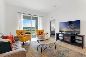 Relax in this stylish living room with a sofa, armchair, and flat-screen TV, offering a view of the outdoors through a large sliding door.