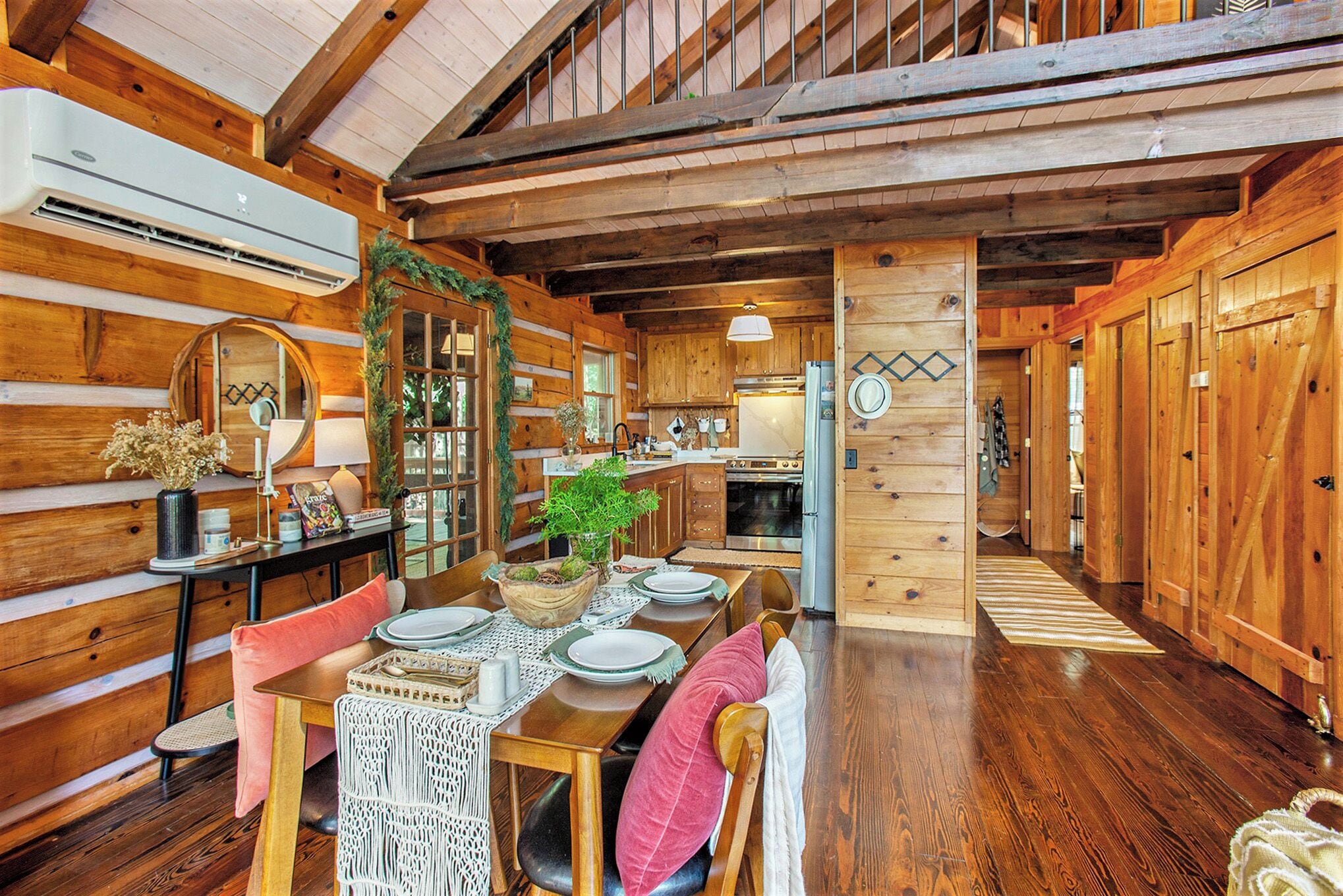 A wooden cabin interior with a dining area, kitchen, and a loft space.