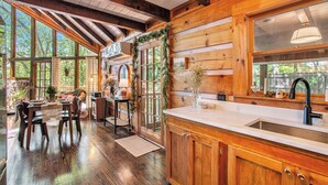 A wooden cabin interior with a dining area, kitchen, and large windows. - Chic Boho Cabin in the Trees! (Ellijay)