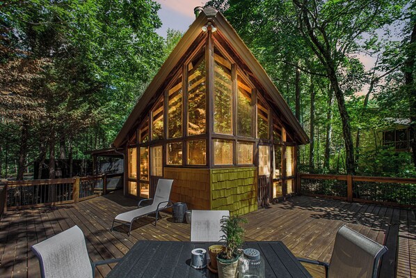 Une cabane en bois dotée de grandes fenêtres, d’une terrasse et de meubles pour s’asseoir à l’extérieur.
