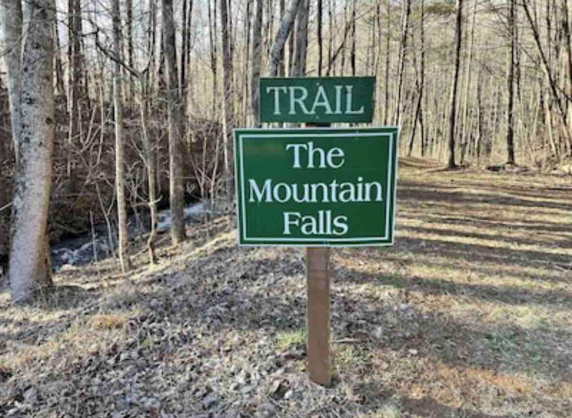 A trail sign for 'The Mountain Falls' in a wooded area.