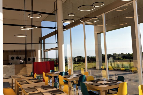 A modern restaurant with large windows, high ceilings, and circular pendant lights.