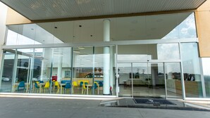 A modern building with large glass windows, a covered entrance, and outdoor seating with yellow and blue chairs. - GoldMen Express Cianorte (Cianorte)