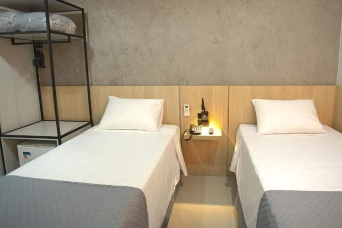 Una habitació d'hotel amb dos llits, una meseta de nit amb un telèfon i una làmpada, i una prestatgeria amb motxilles.