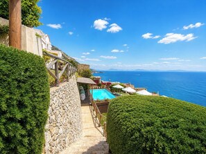 A pool area with a stone wall, wooden deck, and a view of the sea.