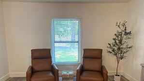 Una habitación con dos sillones de cuero marrón, una mesita de madera, una ventana con persianas y una planta en maceta.