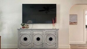 Una consola blanca con tres aberturas circulares, un televisor de pantalla plana encima y una pequeña planta a la izquierda.