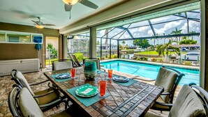 Ein Essbereich mit Blick auf einen Swimmingpool, Deckenventilatoren und einem großen Fenster zum Poolbereich.