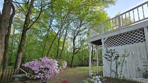 Eine Holzterrasse mit weißer Reling, umgeben von Bäumen und einem Garten mit blühenden Pflanzen.
