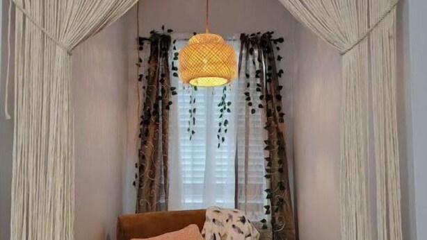 Ein Zimmer mit einem braunen Sofa, einer Pendelleuchte und einem Fenster mit Vorhängen.