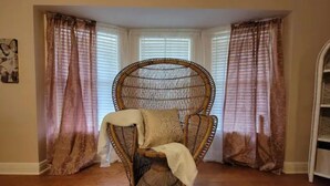 Ein Eckzimmer mit einem großen Korbsessel, einem gemusterten Teppich und einem Fenster mit Jalousien.