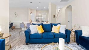 Ein modernes Wohnzimmer mit einem blauen Sofa, einem Couchtisch und einem Essbereich im Hintergrund.