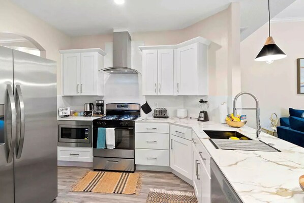 A modern kitchen with white cabinets, stainless steel appliances, a marble countertop, and a built-in oven.