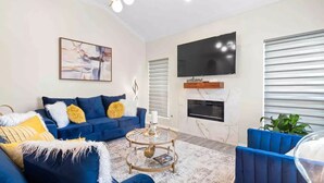 Ein modernes Wohnzimmer mit einem blauen Sofa, einem Couchtisch, einem Flachbildfernseher und einem Kamin.