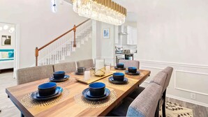Ein Essbereich mit einem langen Holztisch, gedeckt für sechs Personen, einem Chandelier und einer Treppe im Hintergrund.