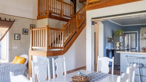 Ein geräumiger Raum mit einer Holztreppe, einem Essbereich mit weißen Stühlen und einer Küchenzeile inklusive Kühlschrank und Herd.