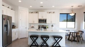 A modern kitchen with white cabinets, stainless steel appliances, and a central island with bar stools. - Home with Four Peaks  and  Mountain views just outside Tonto National Forest 
 (Rio Verde)
