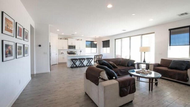 A spacious living area with a kitchen in the background, a large window, and a modern design. - Home with Four Peaks  and  Mountain views just outside Tonto National Forest 
 (Rio Verde)