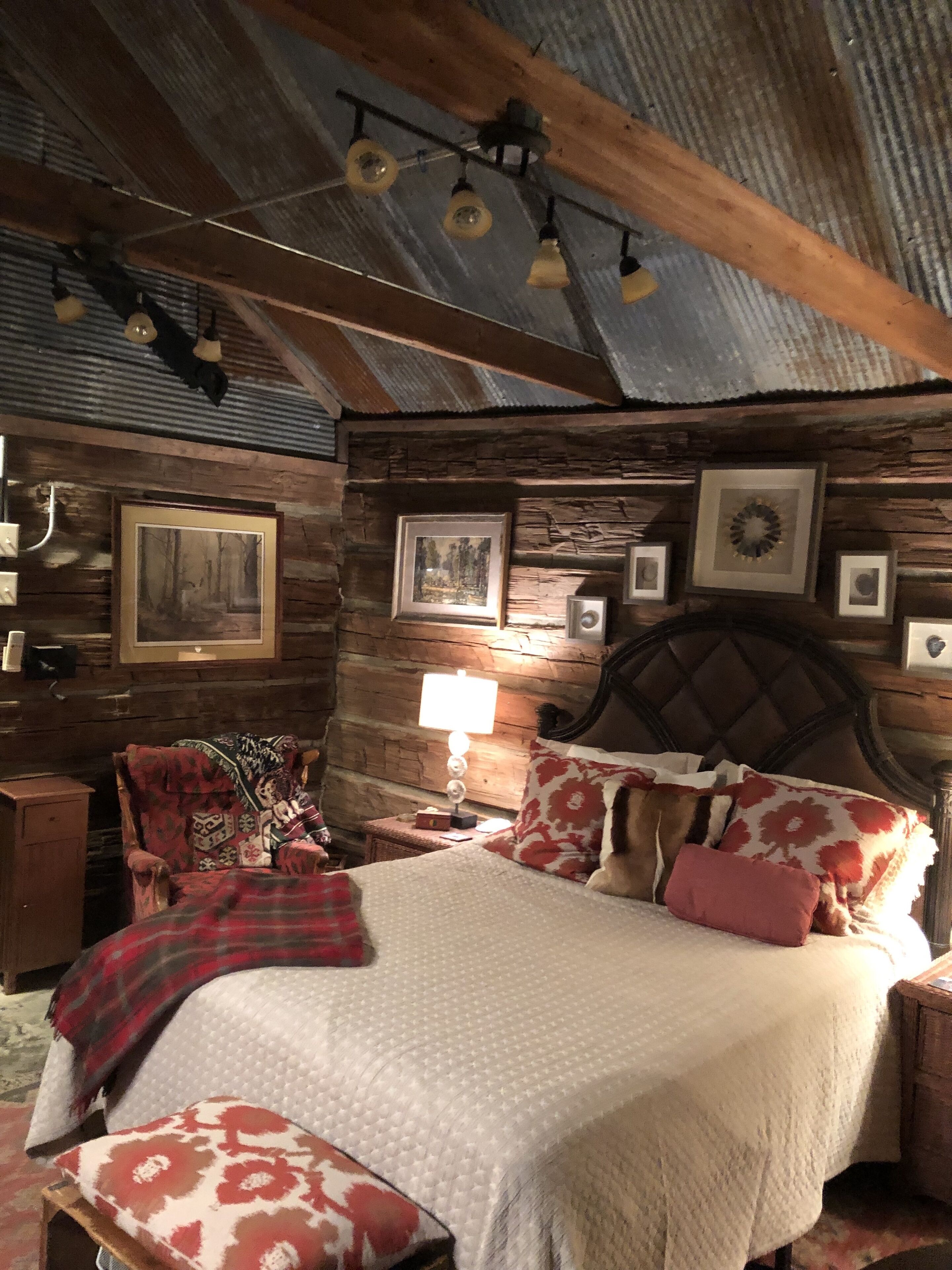A rustic bedroom with a wooden headboard, a bed with patterned bedding, and a nightstand with a lamp.