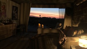 A cozy room with a view of a sunset, wicker furniture, and a wooden ceiling. - Sunset Log Cabin (Clarksdale)