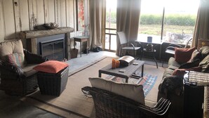 A cozy living room with a fireplace, wicker furniture, and a view of the outdoors. - Sunset Log Cabin (Clarksdale)