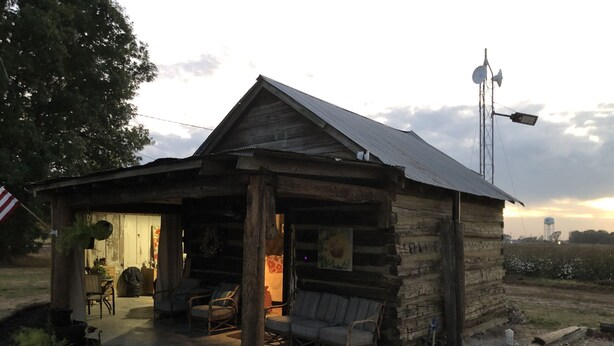 A rustic log cabin with a porch, outdoor seating, and a satellite dish. - Sunset Log Cabin (Clarksdale)