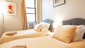 Een hotelkamer met twee bedden, beige beddengoed, een raam met gordijnen en een ingelijst foto aan de muur.