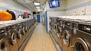 Een wasserette met rijen industriële wasmachines en drogers, een betegelde vloer, en een aan de muur bevestigde televisie.