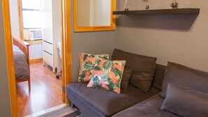 Een knus leefruimte met een bank, twee kussens, een spiegel en een plank met decoratieve objecten.