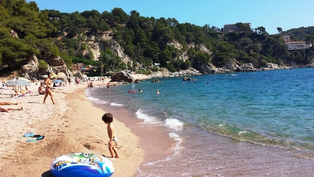 Ein Strand mit klarem, blauem Wasser, Menschen, die sonnenbaden, und ein Kind beim Spielen.