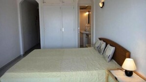 Ein Schlafzimmer mit einem großen Bett, einem Nachttisch mit Lampe, einem Kleiderschrank und einem durch einen Bogen sichtbaren Badezimmer.