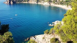 A coastal landscape with clear blue waters, rocky shores, and a hillside with buildings. - Comfortable apartments with swimming pool facing the sea. Ref. Cala Llevadó-46 (Tossa del mar)